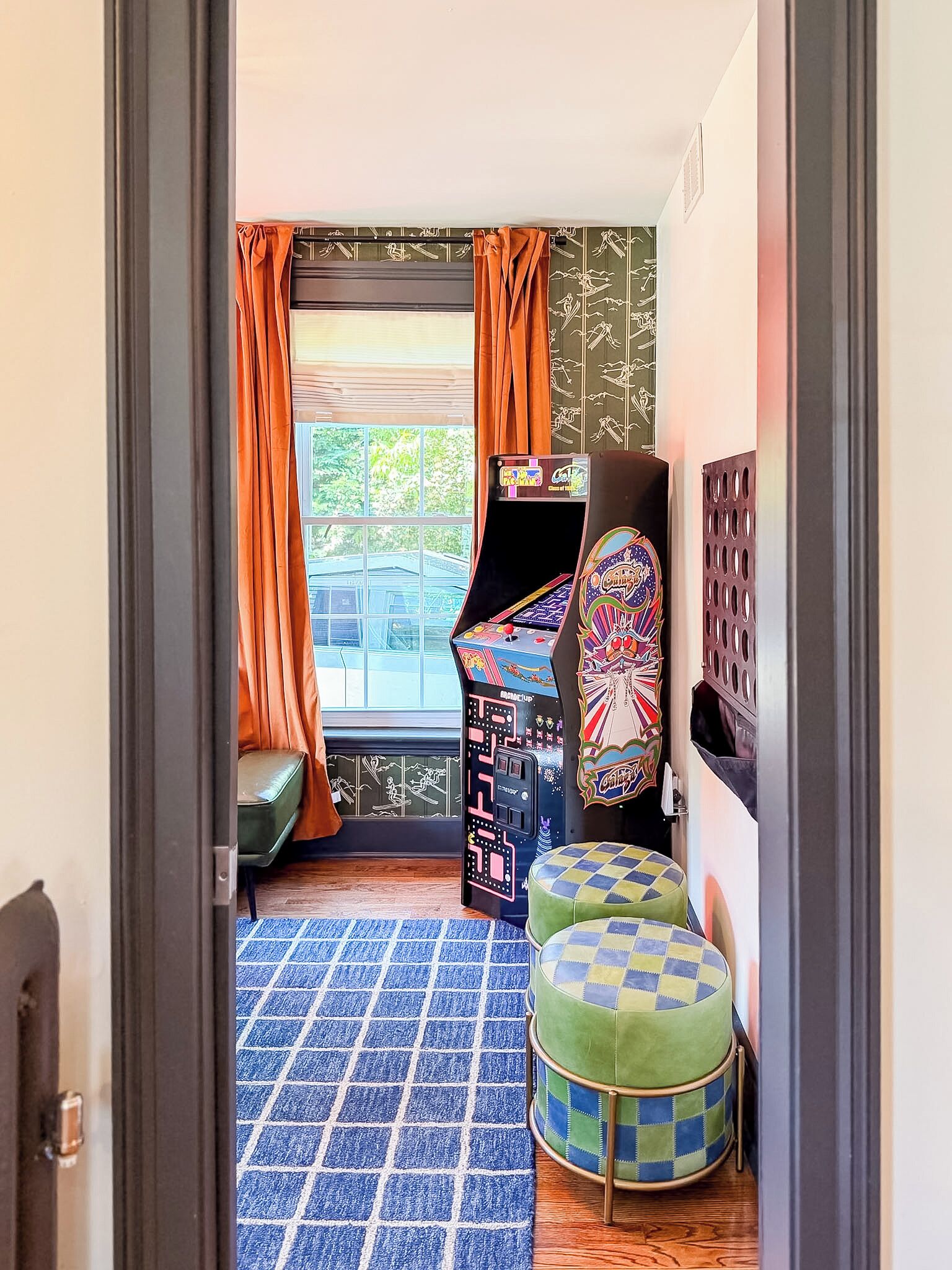 Une pièce avec une fenêtre, un canapé, une petite table et une borne d’arcade aux couleurs vives.