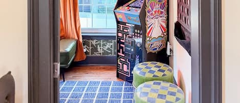 Ein Zimmer mit Fenster, einer Couch, einem kleinen Tisch und einer farbenfrohen Spielmaschine.