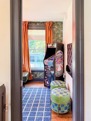 A room with a window, a sofa, a small table, and a colorful arcade machine. - Downtown - Hot Tub, Speakeasy, Grill, Game Room, Fireplace (Ludlow)