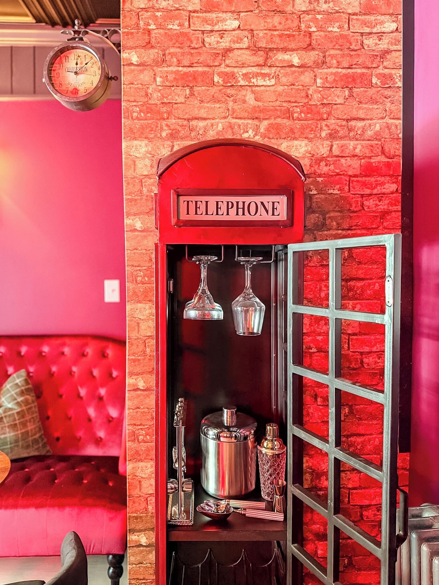 Un mur de briques rouges avec une cabine téléphonique, une horloge et un canapé rouge.