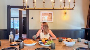 A dining table set with plates, bread, and fruit, under a chandelier. - Downtown - Hot Tub, Speakeasy, Grill, Game Room, Fireplace (Ludlow)