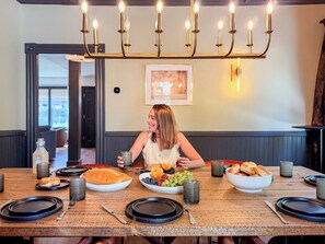 A dining table set with plates, bread, and fruit, under a chandelier. - Downtown - Hot Tub, Speakeasy, Grill, Game Room, Fireplace (Ludlow)