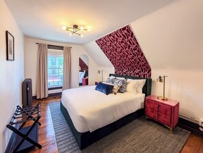 A bedroom with a bed, a red dresser, a mirror, a standing lamp, and a window with curtains. - Downtown - Hot Tub, Speakeasy, Grill, Game Room, Fireplace (Ludlow)