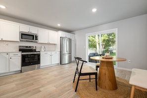 A modern kitchen with white cabinets, stainless steel appliances, and a dining area with a round wooden table and chairs. - New 4 Bed 2 and a Half Bath Near ND Campus (South Bend)