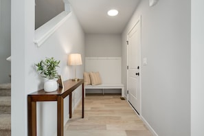 A hallway with a wooden console table, a potted plant, a bench, and a wall-mounted lamp. - New 4 Bed 2 and a Half Bath Near ND Campus (South Bend)