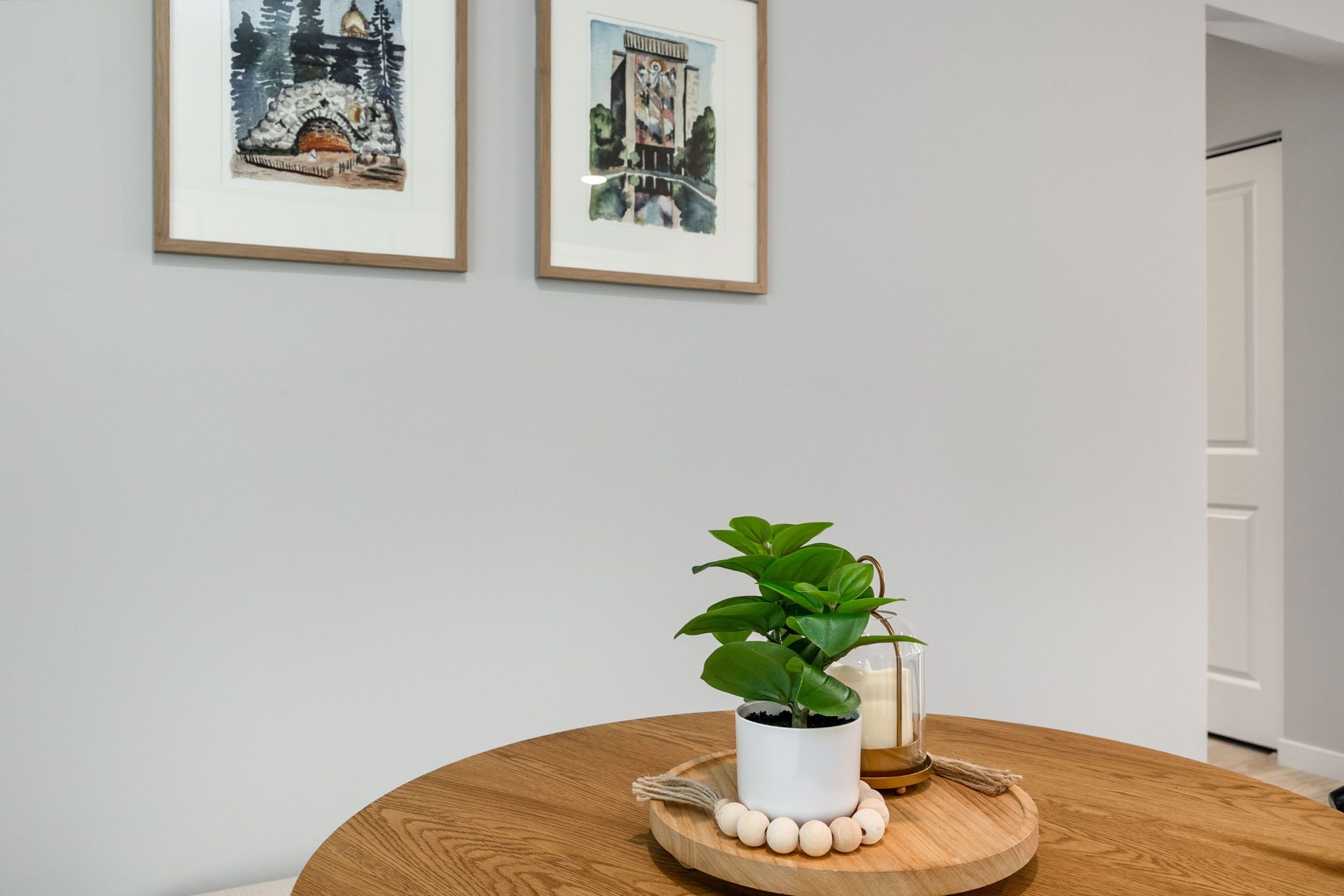 Ein Zimmer mit einem runden Holztisch, einer Topfpflanze und zwei gerahmten Kunstwerken an der Wand.