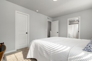 Un dormitorio con una cama grande, dos puertas, una silla y una zona de ducha.