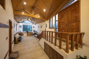 Un intérieur spacieux avec un escalier en bois, un espace d’accueil et de grandes fenêtres offrant une vue dégagée.