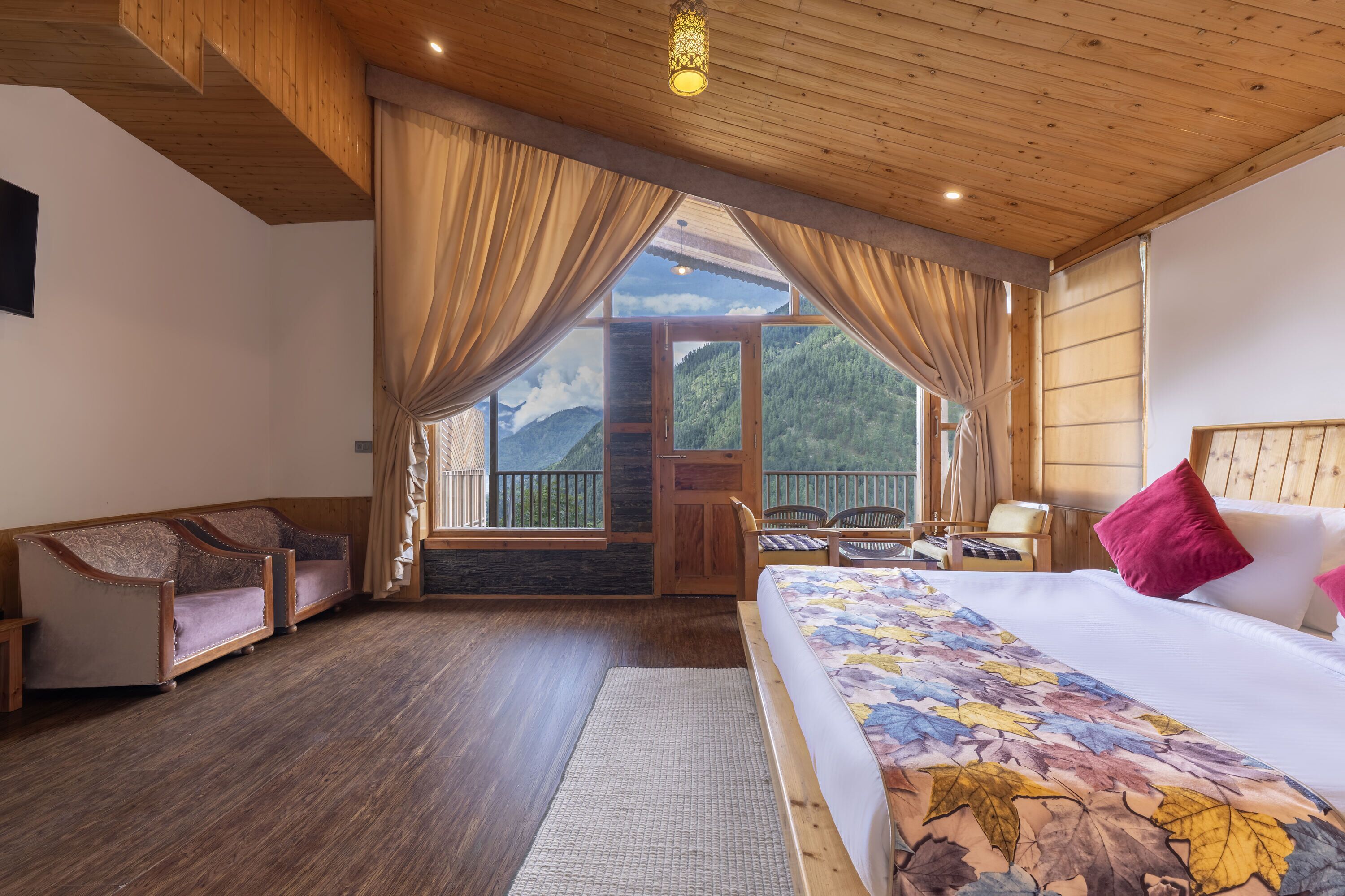 A hotel room with a large bed, a wooden ceiling, and a view of mountains through the window.