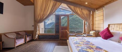 A hotel room with a large bed, a wooden ceiling, and a view of mountains through the window.