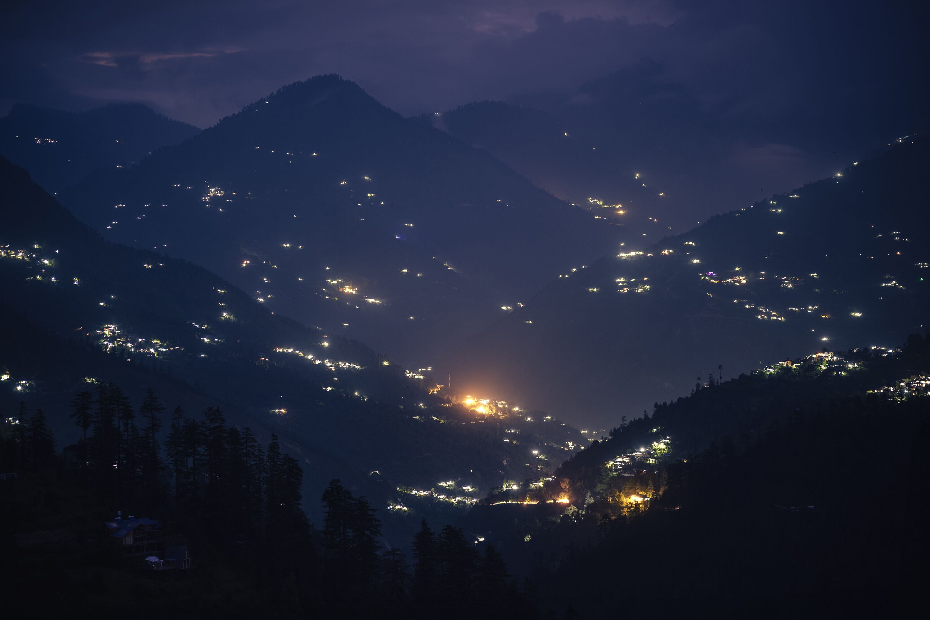 A mountainous landscape at night with scattered lights indicating settlements.
