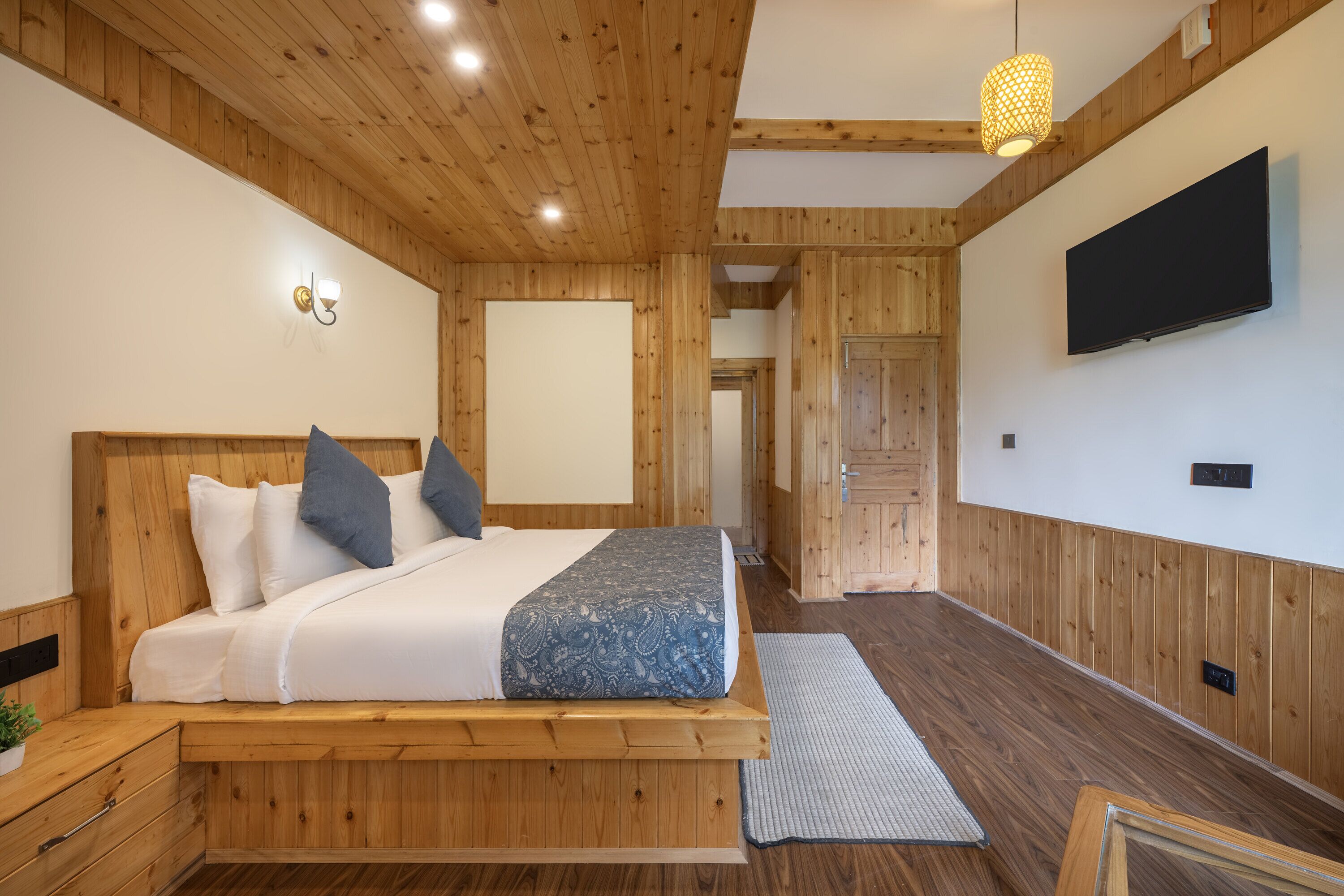 A bedroom with a wooden bed, a television on the wall, and a hallway leading to another room.