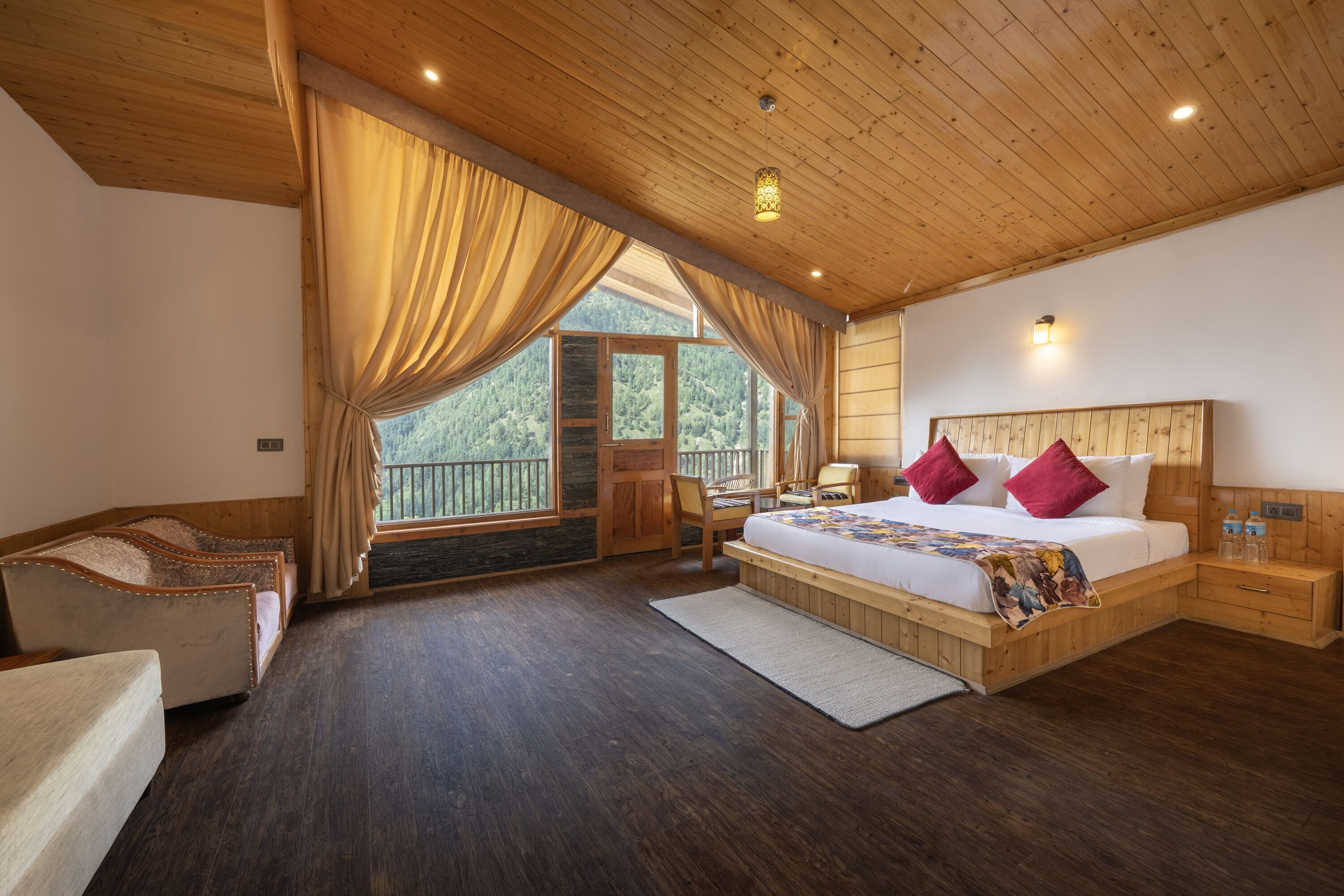 Un dormitorio con una cama grande, cabecera de madera, una mesita de noche, una silla, una ventana con cortinas y vistas al exterior.