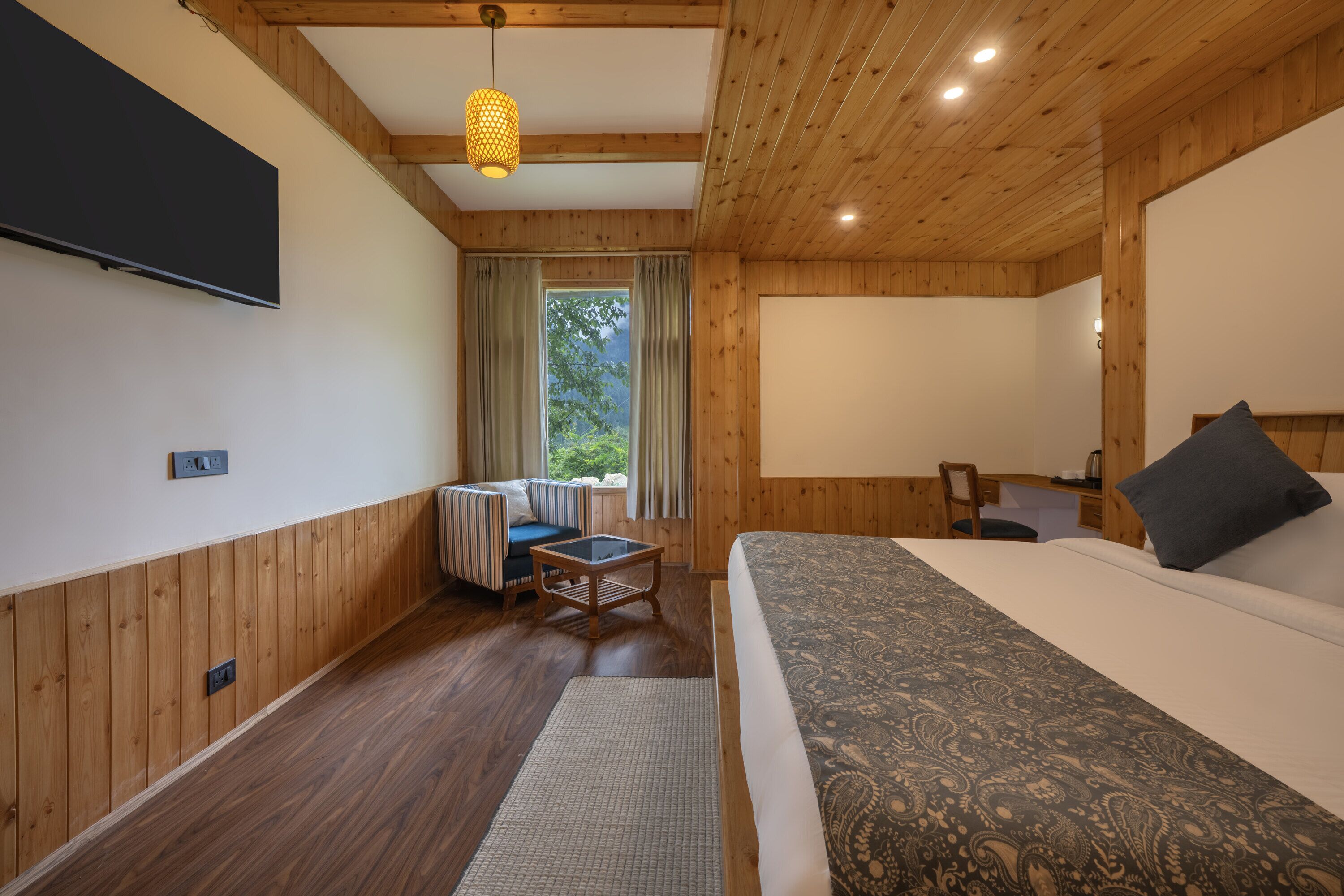 Una habitación con paneles de madera, una cama, un escritorio, una silla, un televisor y una ventana con cortinas.