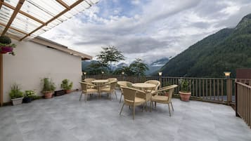 A terrace with outdoor furniture and potted plants, overlooking a mountainous landscape.