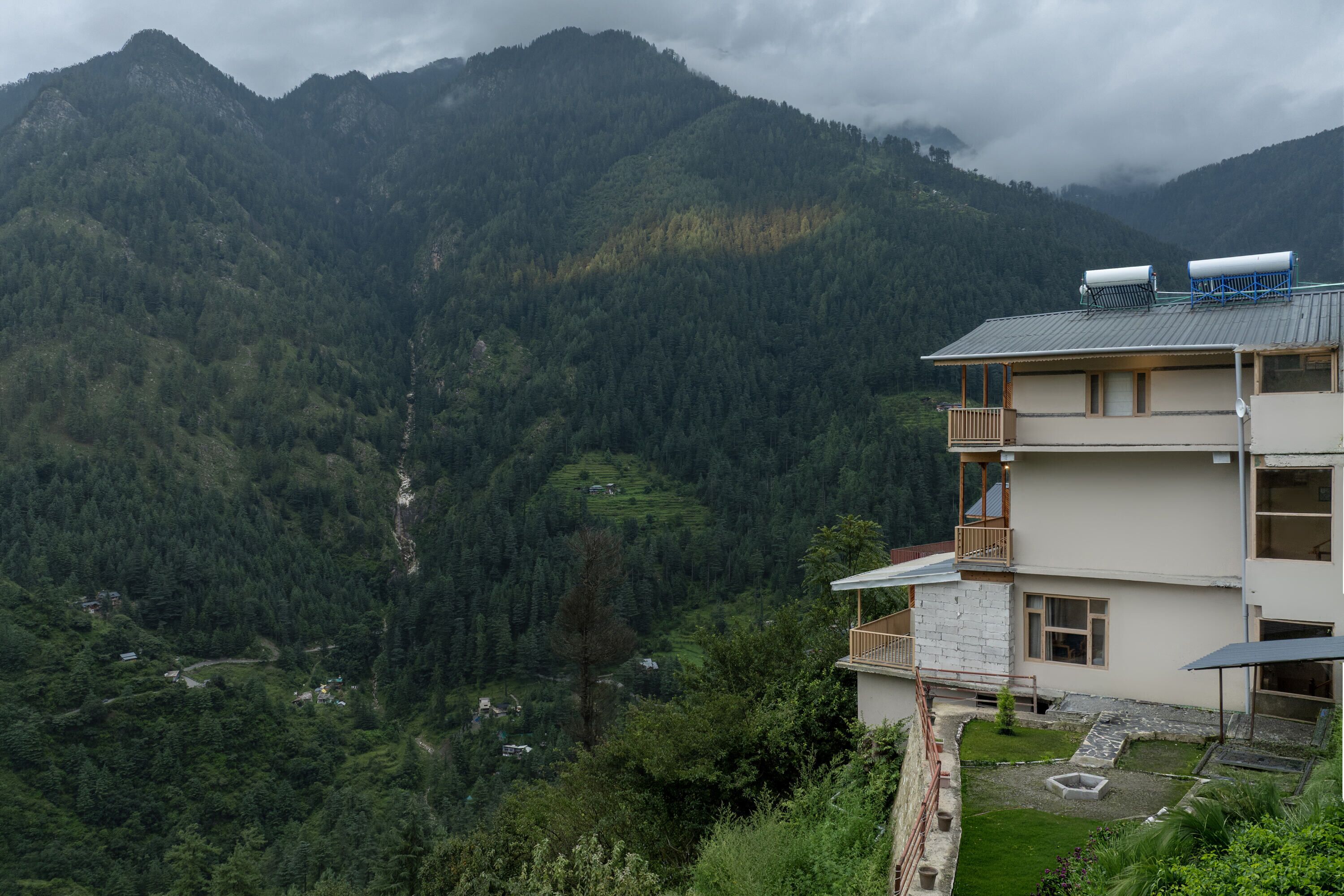 A multi-story building with a balcony, surrounded by lush green mountains and a valley.