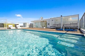 Ein Schwimmbecken mit Liegestühlen und einer überdachten Sitzgelegenheit.