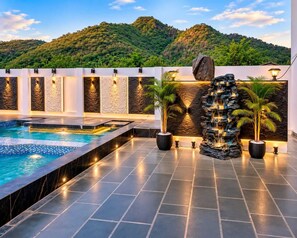 Una piscina con una cascada, rodeada de muros de piedra y plantas en macetas, con vistas a un paisaje montañoso.