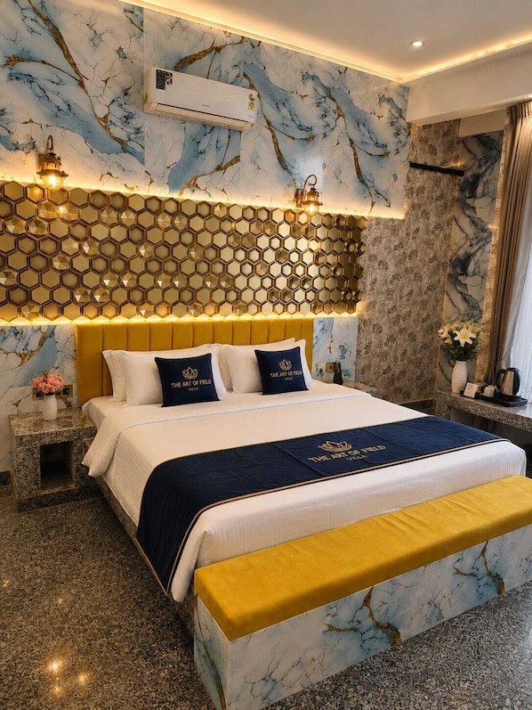 Una habitación de hotel con pared de diseño marmolizado, una lámpara de forma hexagonal, una cama con cabecera amarilla y un banco.