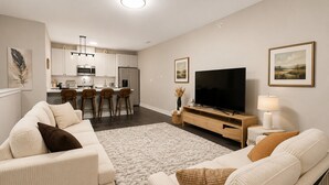 A modern living room with a sofa set, a flat-screen TV, and a dining area with bar stools.