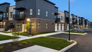 A modern residential building with a flat roof, multiple balconies, and a well-maintained lawn.
