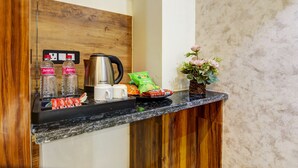 A kitchen counter with a coffee maker, two mugs, a bottle of water, a packet of snacks, and a potted plant. - Hotel Signature Suites (New Delhi)