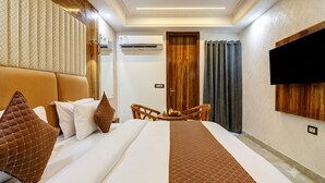 A hotel room with a bed, a television mounted on the wall, a small table with fruits, and a wooden door. - Hotel Signature Suites (New Delhi)