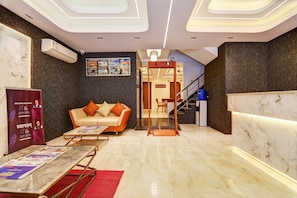 A modern hotel lobby with marble flooring, a sofa, a reception desk, and a staircase. - Hotel Signature Suites (New Delhi)
