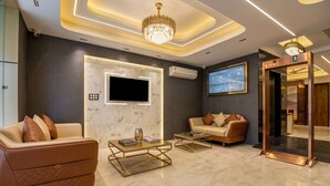 A modern hotel lobby with a marble floor, leather sofas, a flat-screen TV, and a chandelier. - Hotel Signature Suites (New Delhi)