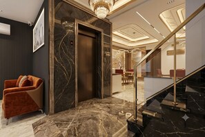 A modern elevator with a marble wall, a red upholstered chair, and a staircase with a glass railing. - Hotel Signature Suites (New Delhi)