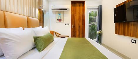 Habitación de hotel con una cama, alfombra verde, puerta de madera, televisor montado y ventana con vistas a zonas verdes.