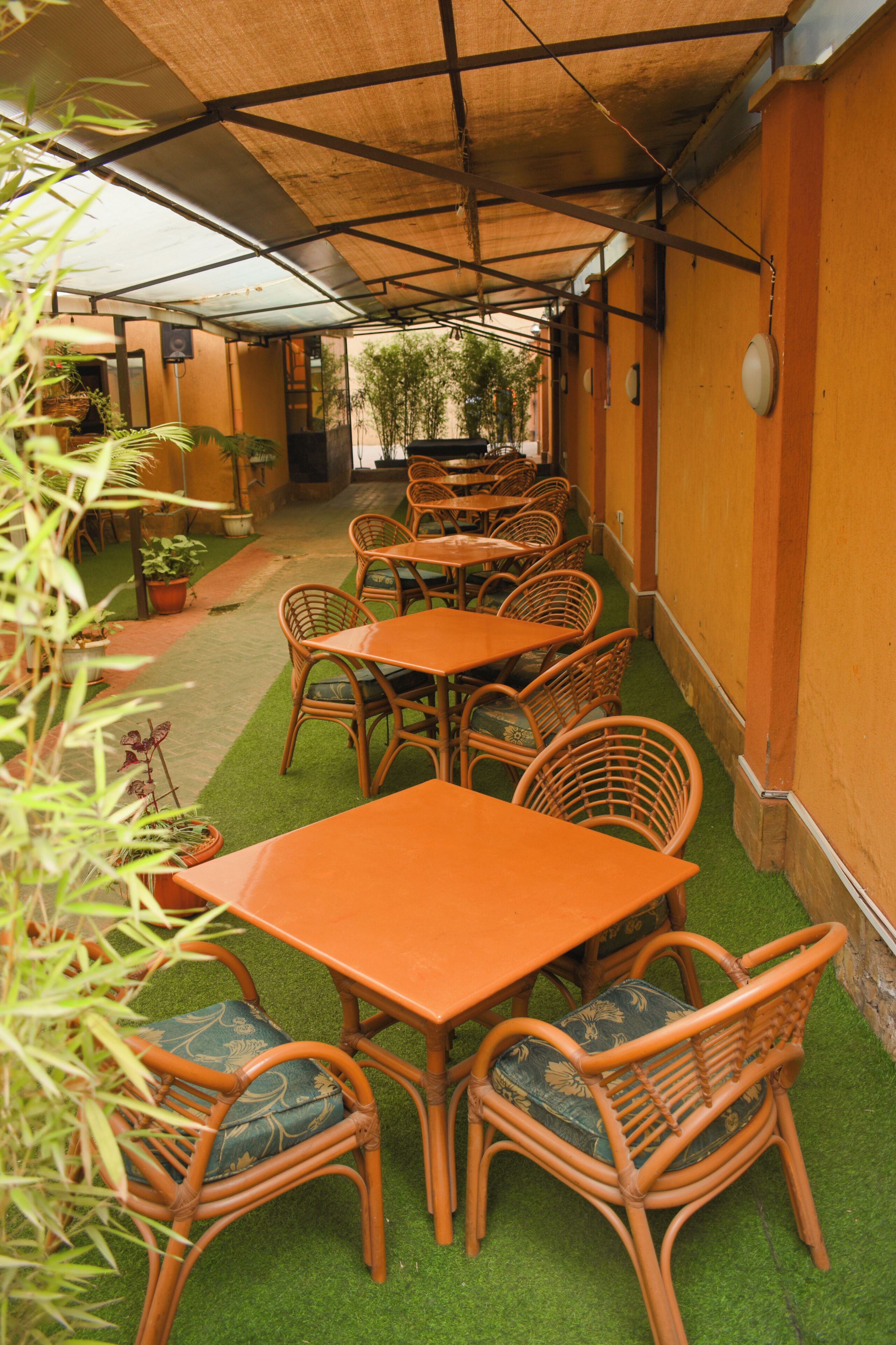 Un espace extérieur aménagé avec des tables et des chaises en osier, entouré de murs et de plantes en pot.
