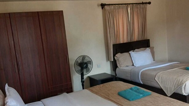 A hotel room with two beds, a wardrobe, a fan, and a curtain. - Jp Resort & Spa (Nairobi)