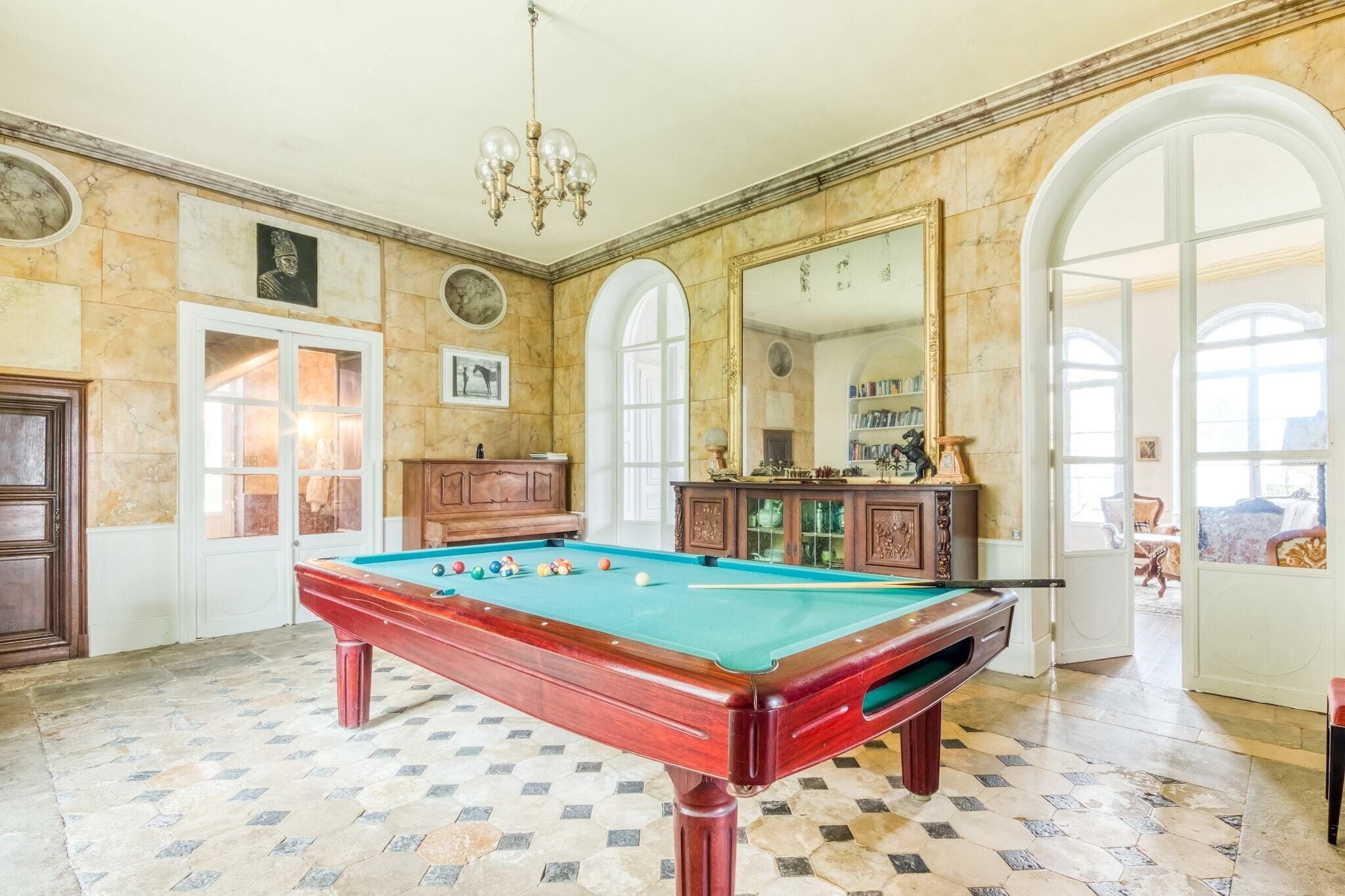 A pool table in a room with marble walls, a chandelier, and a large mirror.