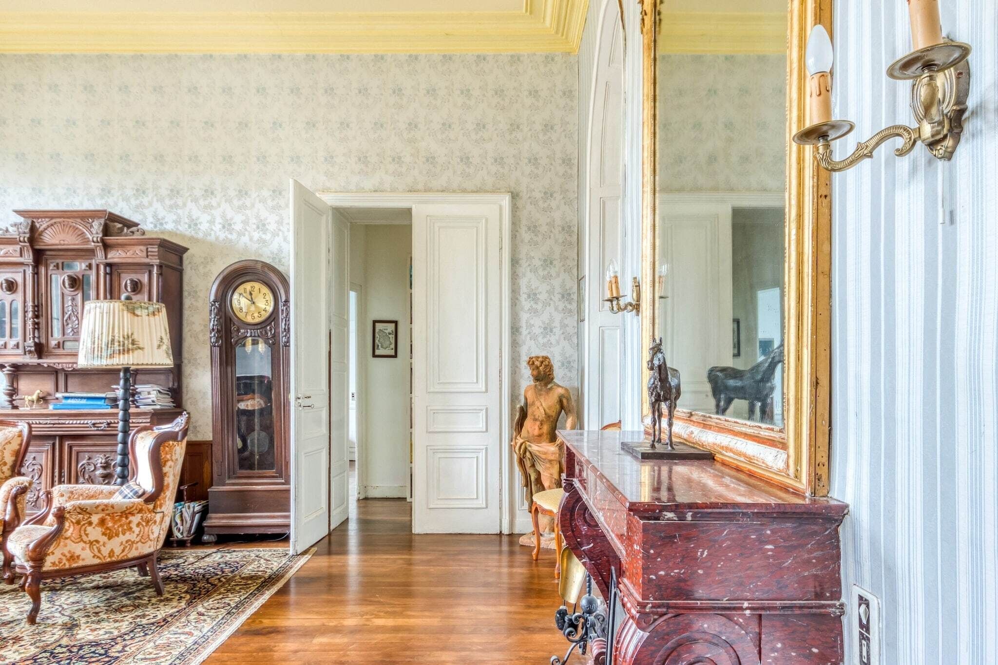 Una habitación con un armario de madera, un espejo grande, una estatua y una puerta que da a otra habitación.