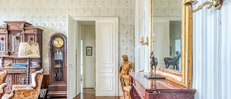 Habitació amb un armari de fusta, un gran mirall, una estàtua i una porta que condueix a una altra habitació.