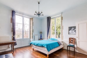 A bedroom with a bed, a chair, a table, a lamp, and a window.