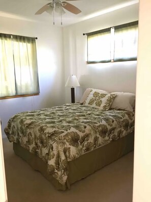 Ein Schlafzimmer mit einem Bett, einem Deckenventilator, einem Fenster mit Vorhängen und einer Nachttischlampe.