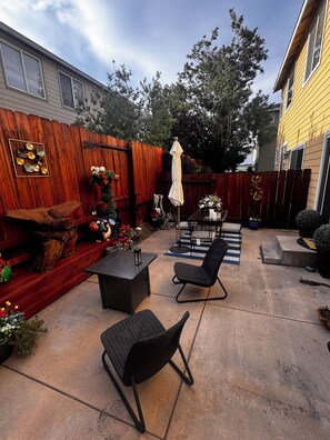 Une terrasse à l’arrière de la maison, avec une table et des chaises, une clôture en bois et un mur décoratif.