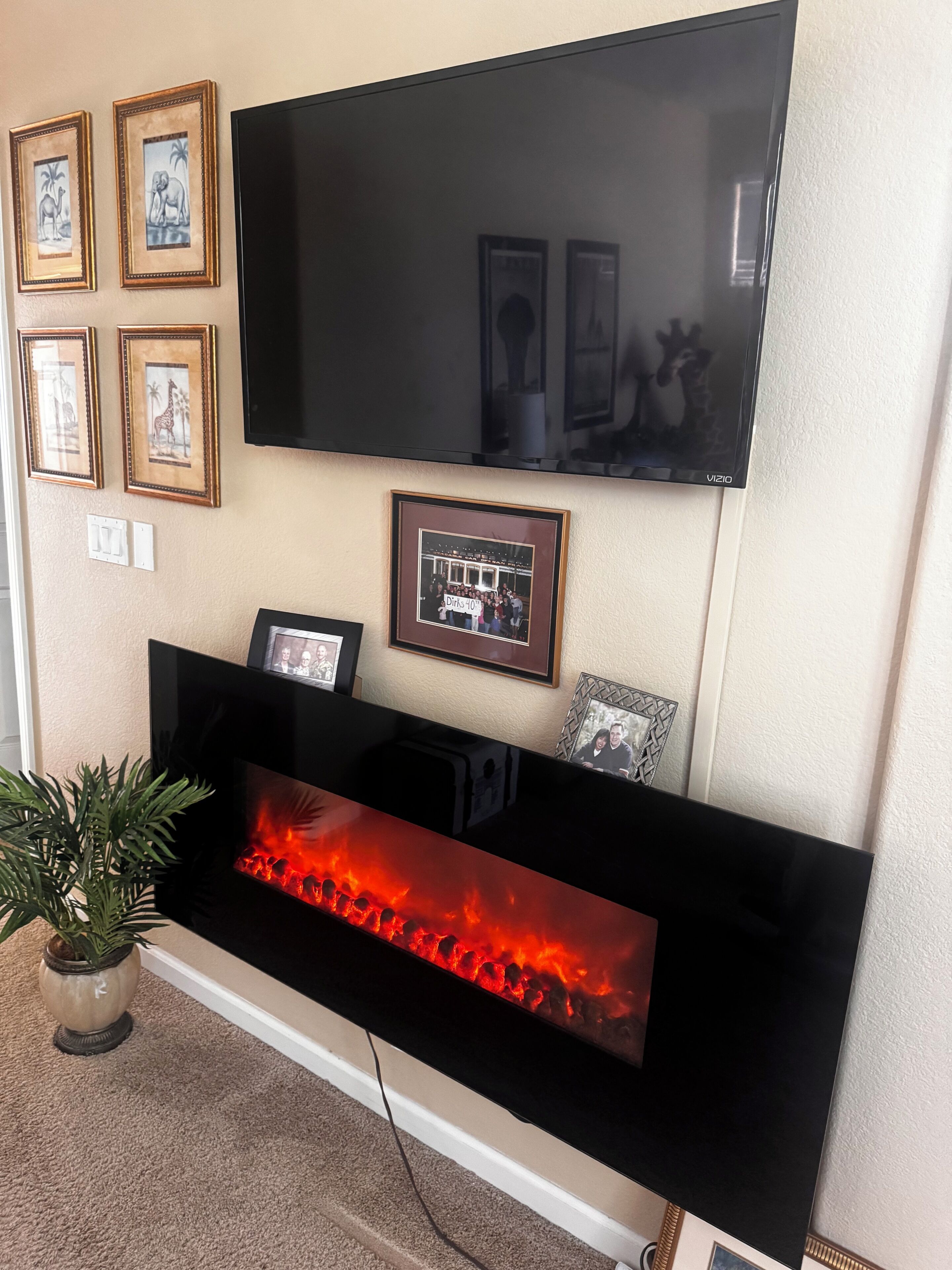 Una sala de estar con un televisor de pantalla plana montado en la pared, una chimenea debajo y varias fotografías enmarcadas en la pared.