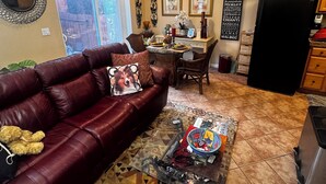 En opholdsstue med en lædersofa, et sofabord med magasiner og et spiseområde med bord og stole.