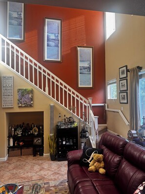 A living room with a staircase, a leather sofa, a teddy bear, and a wine rack with bottles. - Charming 3-bedroom house  in quaint and quiet Reno neighborhood, (Reno)