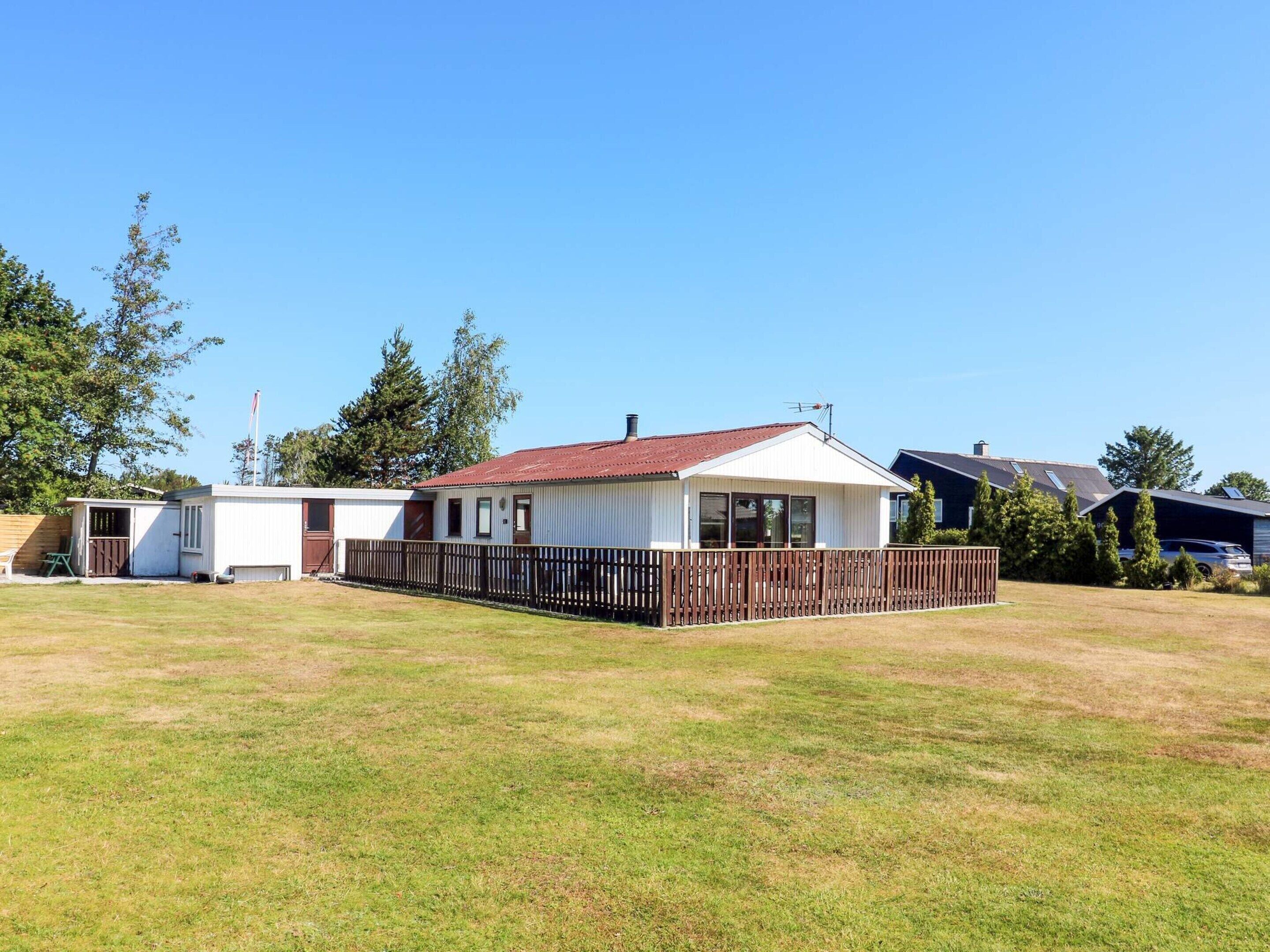Une maison mobile de plain-pied avec une cour clôturée, un petit garage attenant et un ciel dégagé.
