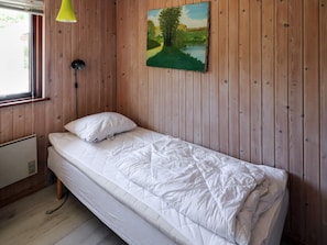 Ein Einzelbett mit weißer Matratze und Kissen in einem Zimmer mit Holzwänden.