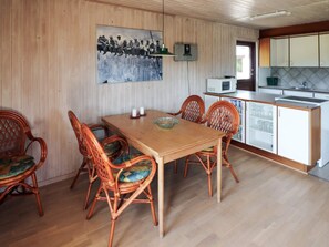 A dining area with a wooden table and wicker chairs, a kitchen with white cabinets and a microwave, and a cityscape painting on the wall. - 5 Person Holiday Home in Hadsund (Hadsund)