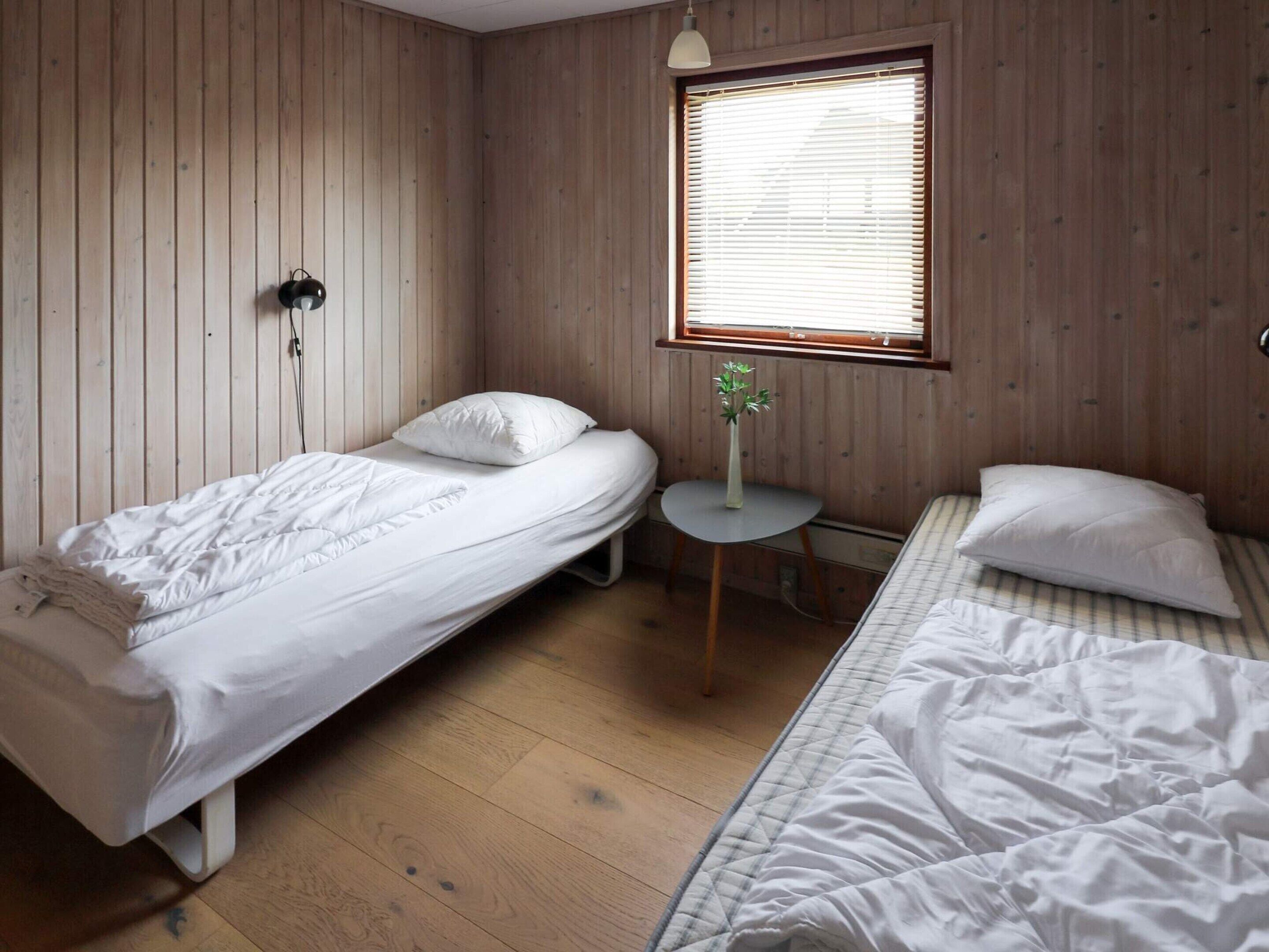 Una habitación con dos camas individuales, una mesita redonda y una ventana con persianas.