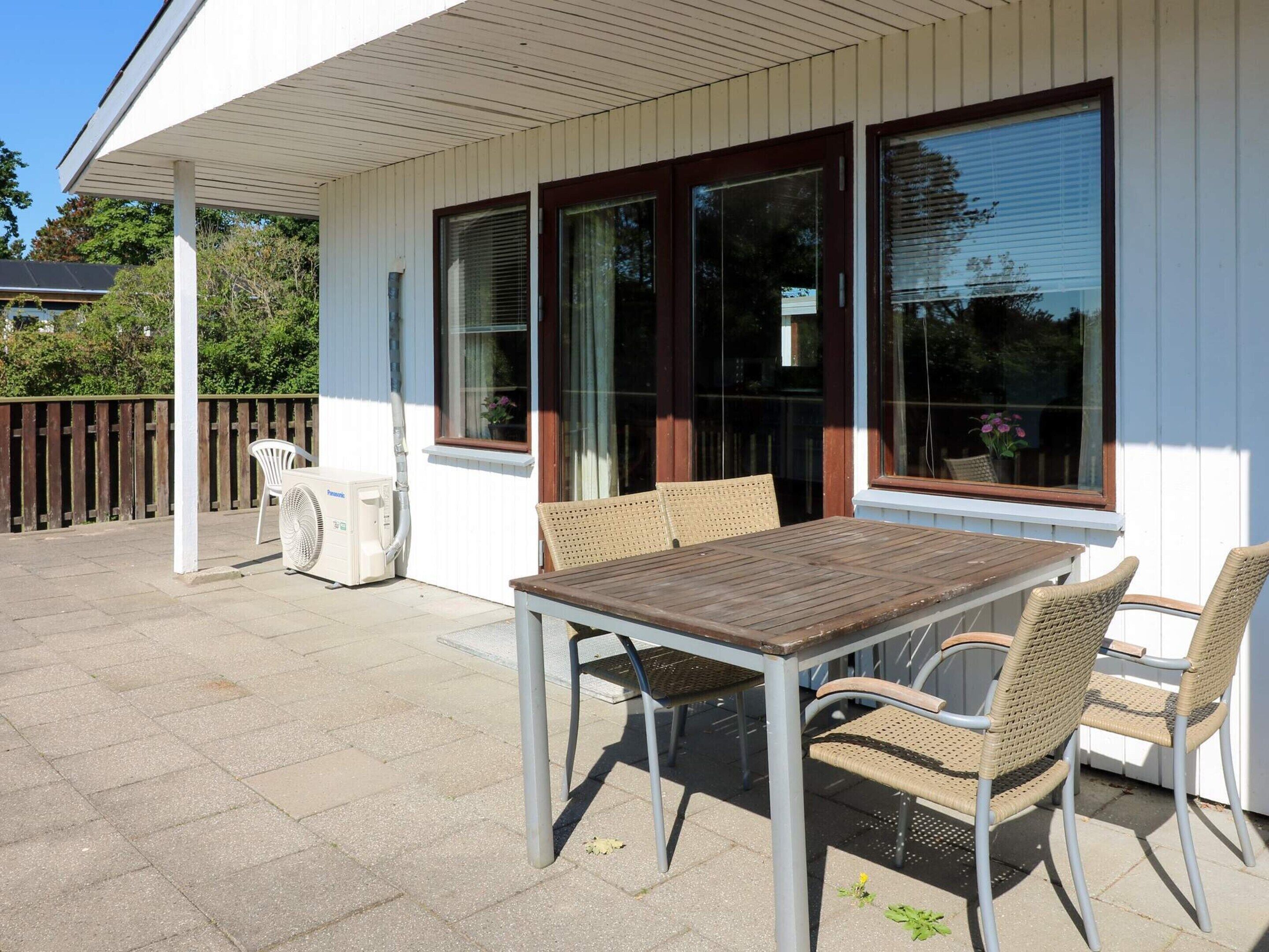 An outdoor patio with a table and chairs, a fan, and a window with blinds.
