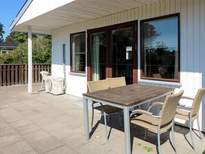 Eine Terrasse im Freien mit Tisch, Stühlen, einem Ventilator und einem Fenster mit Jalousien.