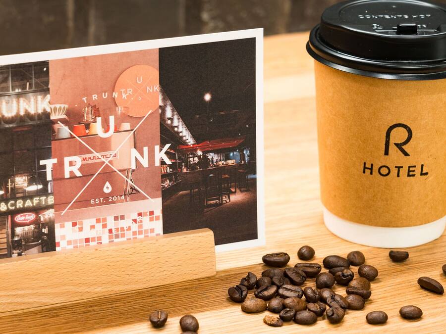 A coffee cup with a logo, a business card, and scattered coffee beans on a wooden surface.