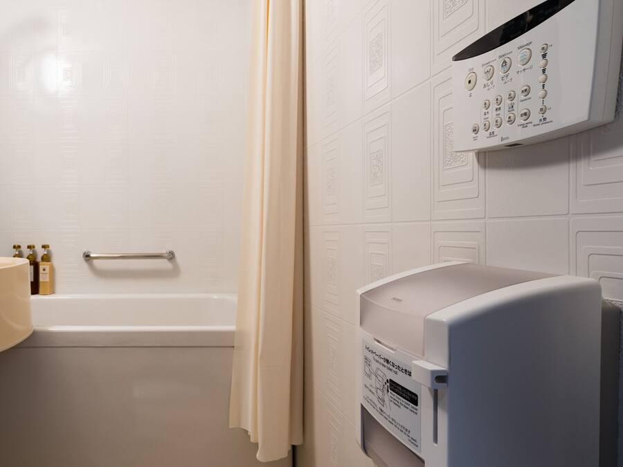 A bathroom with a bathtub, a shower, and a toilet. There is a towel rack and a soap dispenser on the wall.